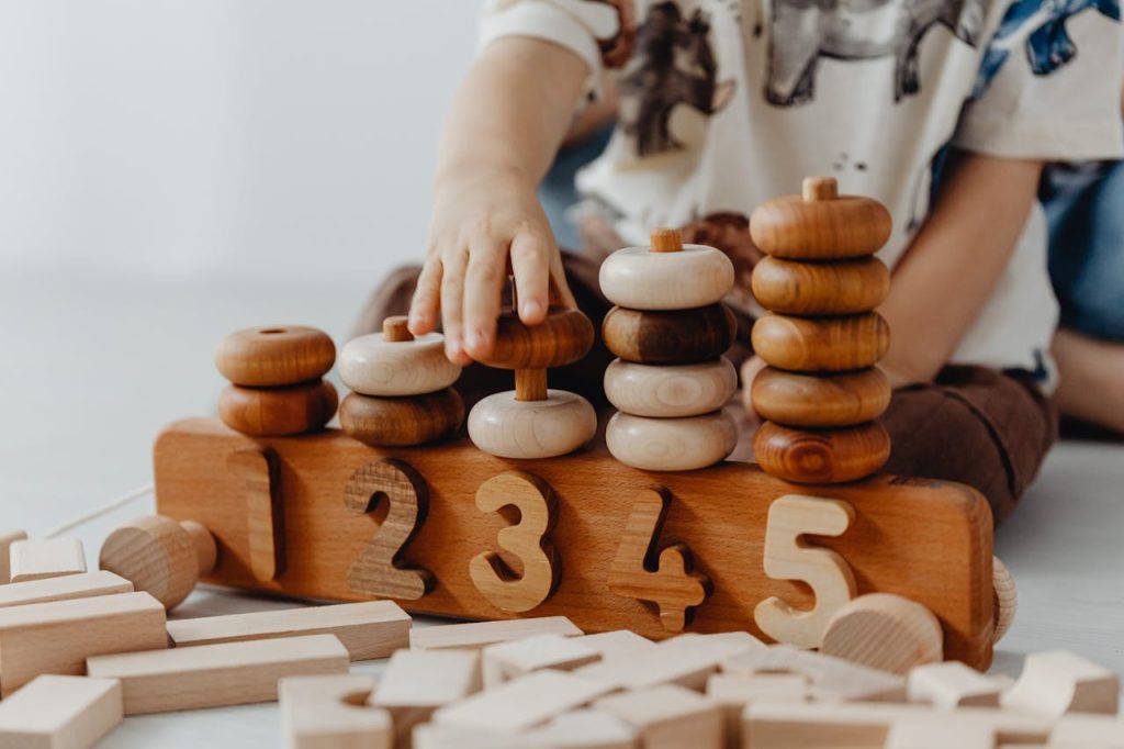 pexels-photo-7269674 Child's hand interacting with wooden educational toys and number blocks indoors.
