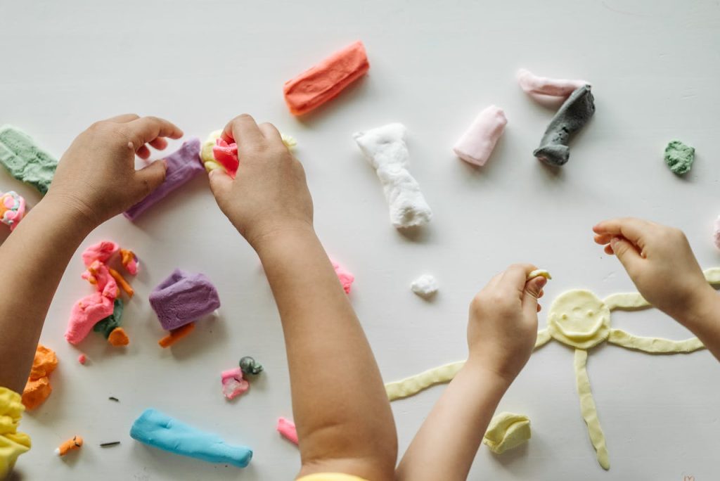 pexels-photo-8422174 Children engaged in creative clay play, forming shapes and exploring colors on a white table.